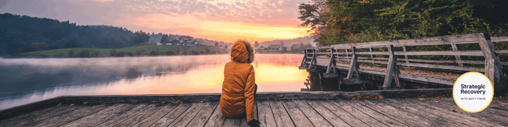 Person sitting peacefully by a lake at sunrise, symbolizing the nervous system’s return to safety and regulation.