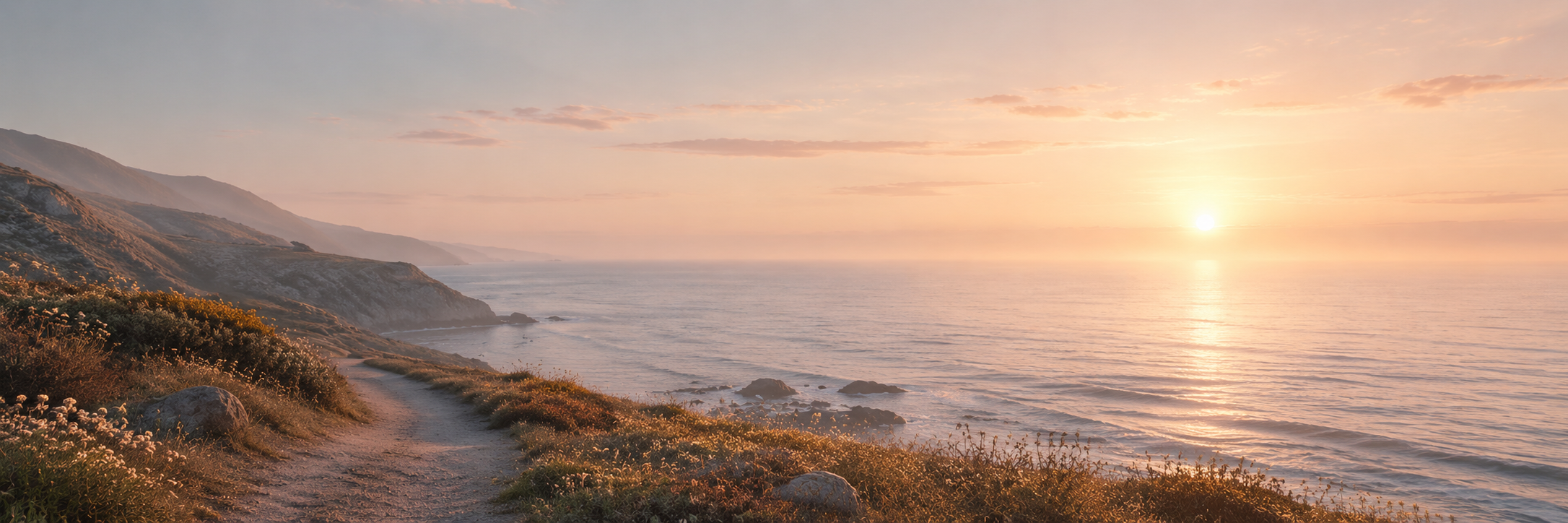 Golden sunrise over a quiet coastal path beside the ocean, with warm light reflecting across gentle waves.